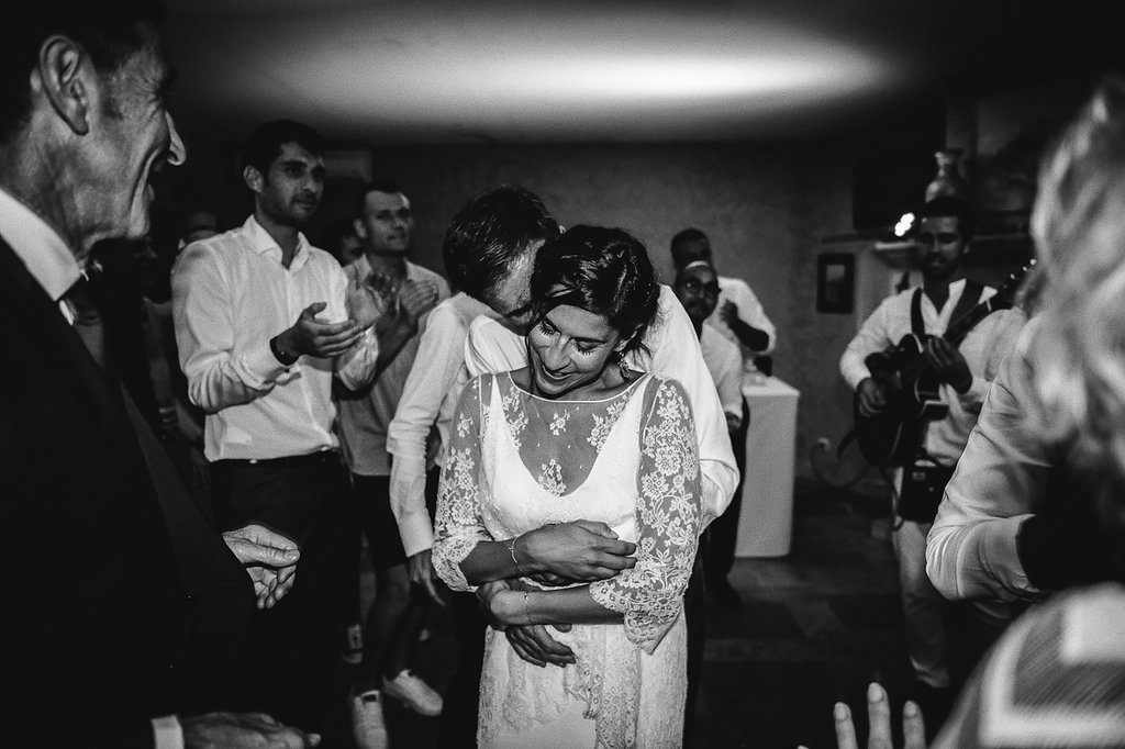 Bride in lace wedding dress surrounded by guests at wedding reception in black and white photo.