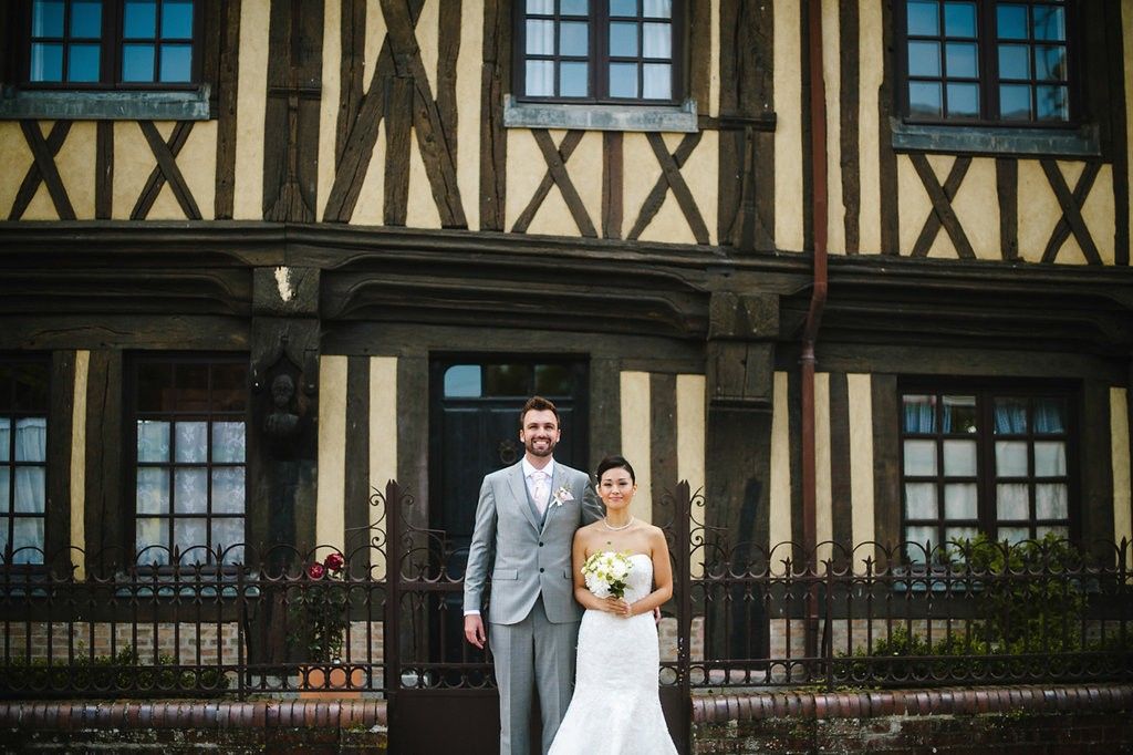 A bride and groom pose together in front of a classic Tudor-style building with timber framing on their wedding day.