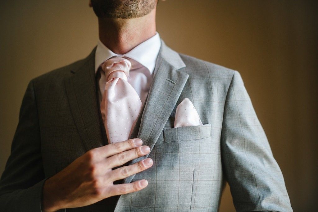 Groom in gray suit with pink tie and pocket square adjusting jacket before wedding.