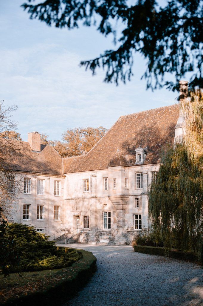 Elegant French chateau surrounded by lush trees and manicured gardens on a sunny autumn day.