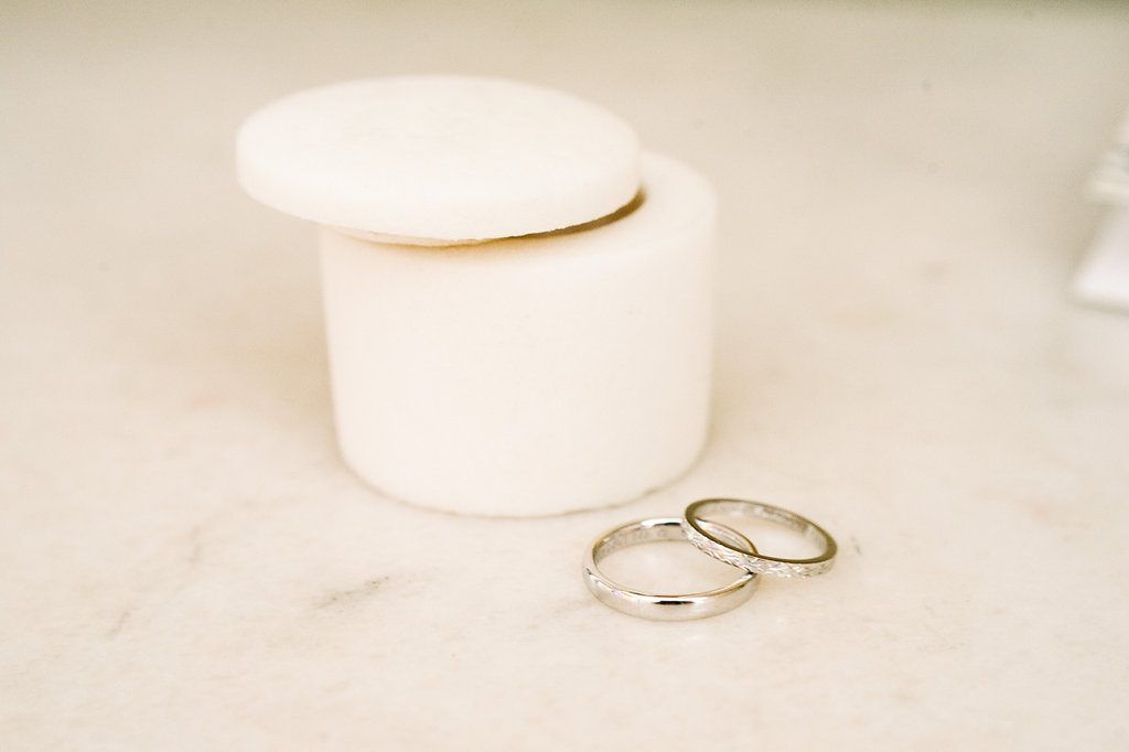 Two gold wedding bands placed beside a small white marble ring box.
