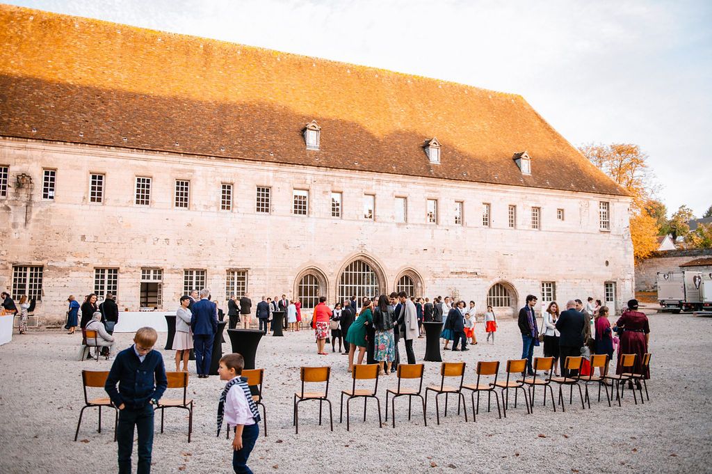 Wedding guests mingling outside a large historic stone building with chairs arranged nearby.