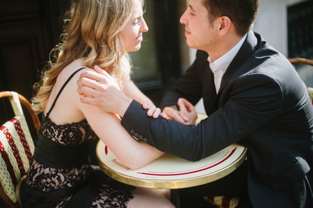 Couple sitting close together at a Parisian cafe table, sharing an intimate and romantic moment.