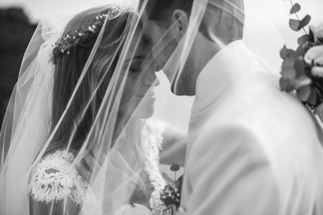 Black and white photo of bride and groom sharing a romantic moment under a wedding veil.