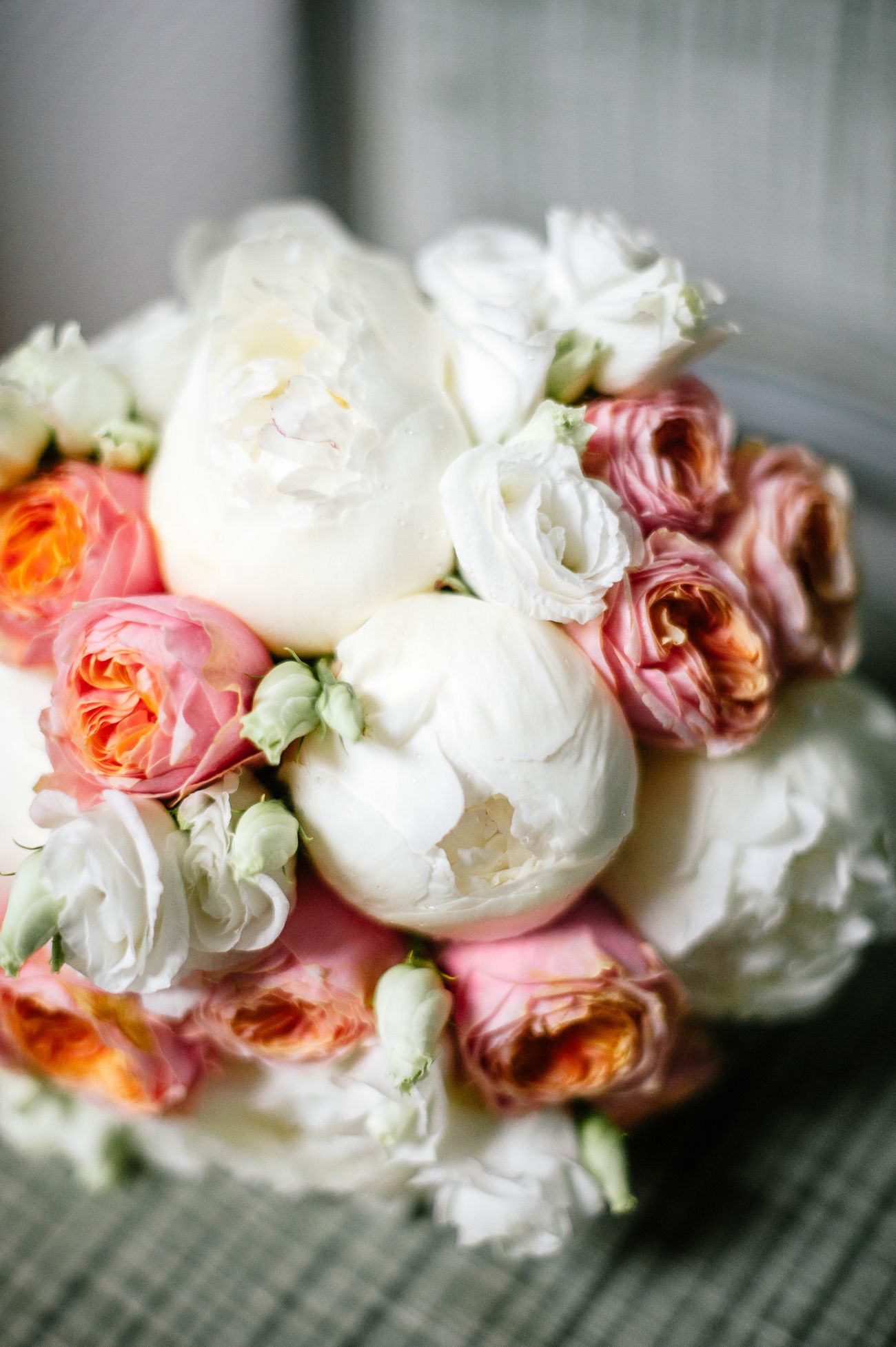 Elegant bridal bouquet featuring white peonies and pink garden roses with orange accents.