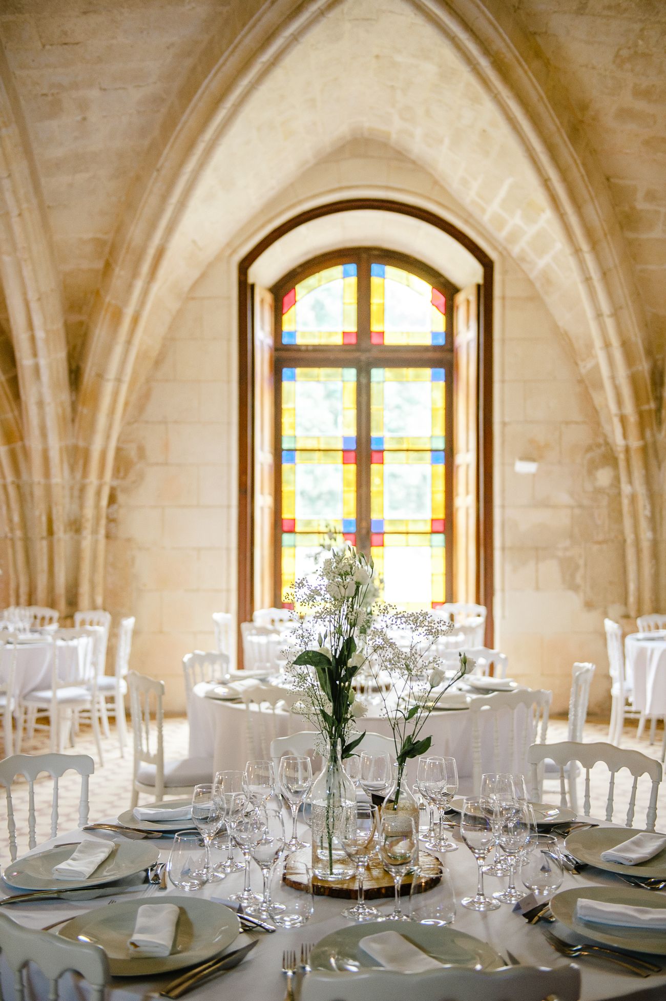Elegant wedding reception hall with gothic arches, stained glass window, and white table settings.