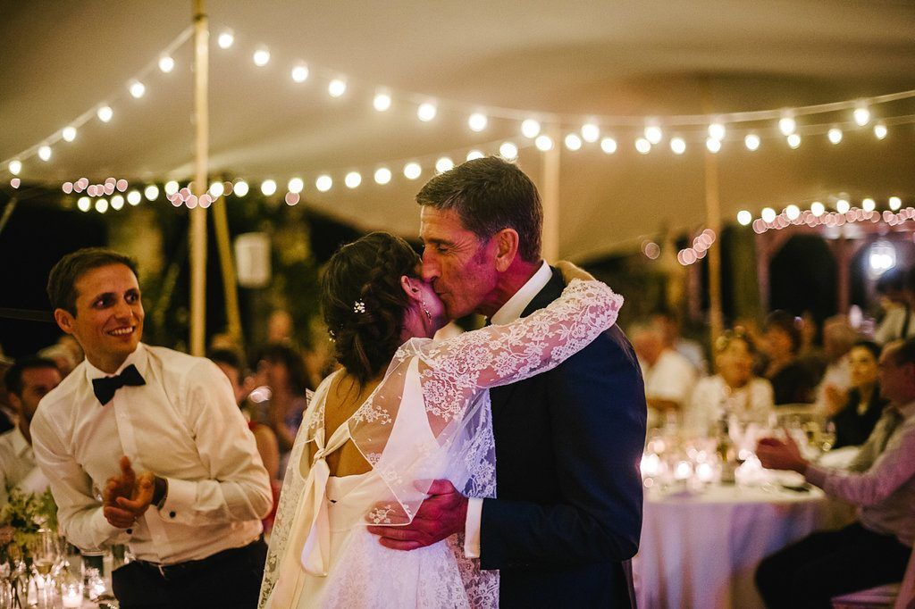 Bride and groom sharing romantic kiss on dance floor under warm string lights.