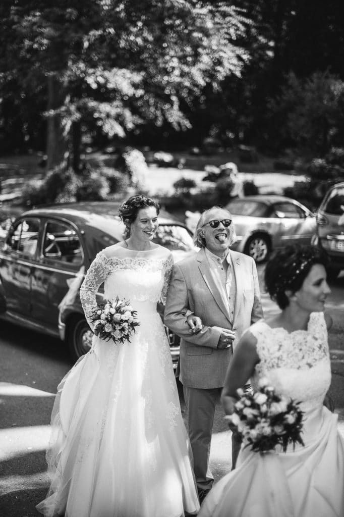 Black and white photo of two brides walking with an escort carrying bouquets outdoors.