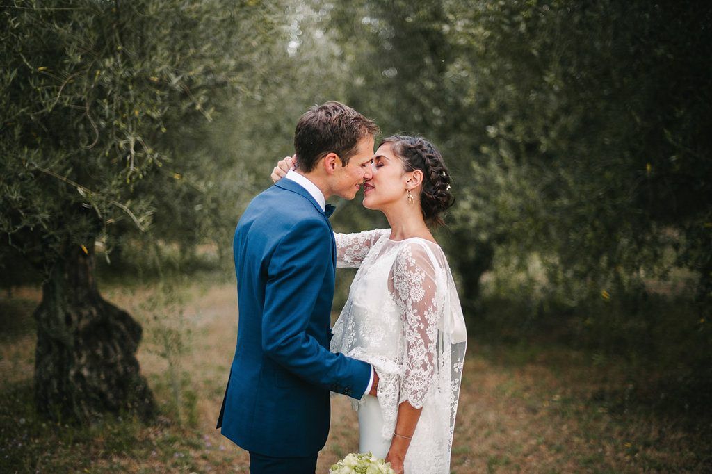 Bride and groom share a romantic kiss among ancient olive trees in the French countryside after wedding ceremony.