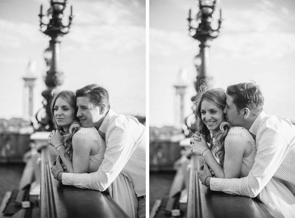 Black and white photo of a couple embracing romantically on a bridge in Paris.
