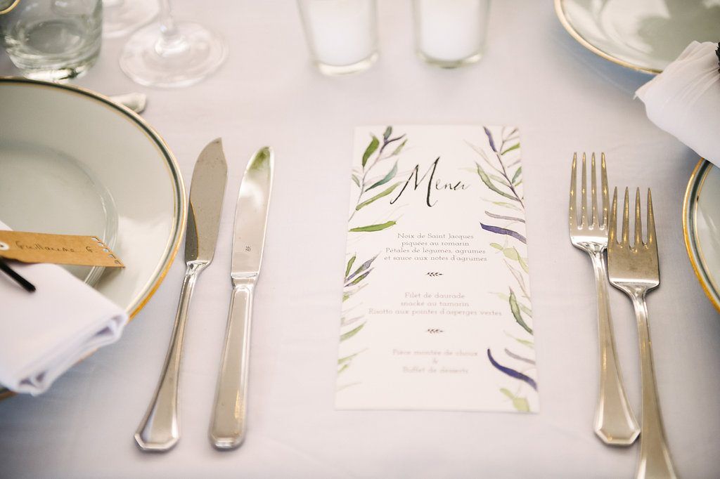 Elegant wedding place setting with silver cutlery, gold-rimmed plates, and botanical watercolor menu card.