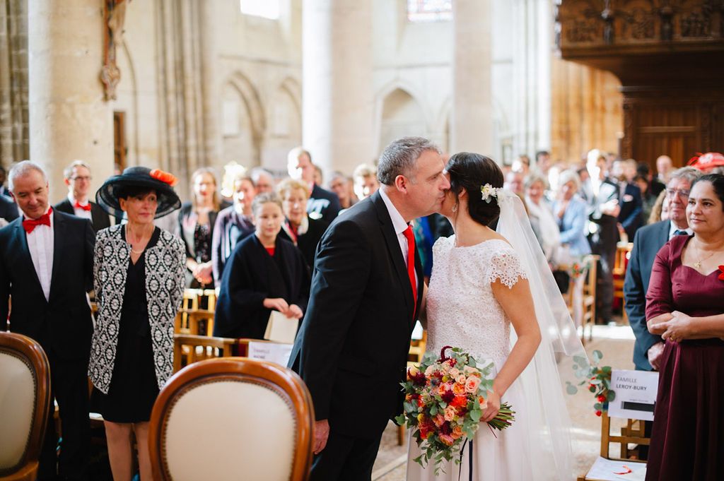 Father of bride sharing a kiss with daughter at church wedding ceremony altar.