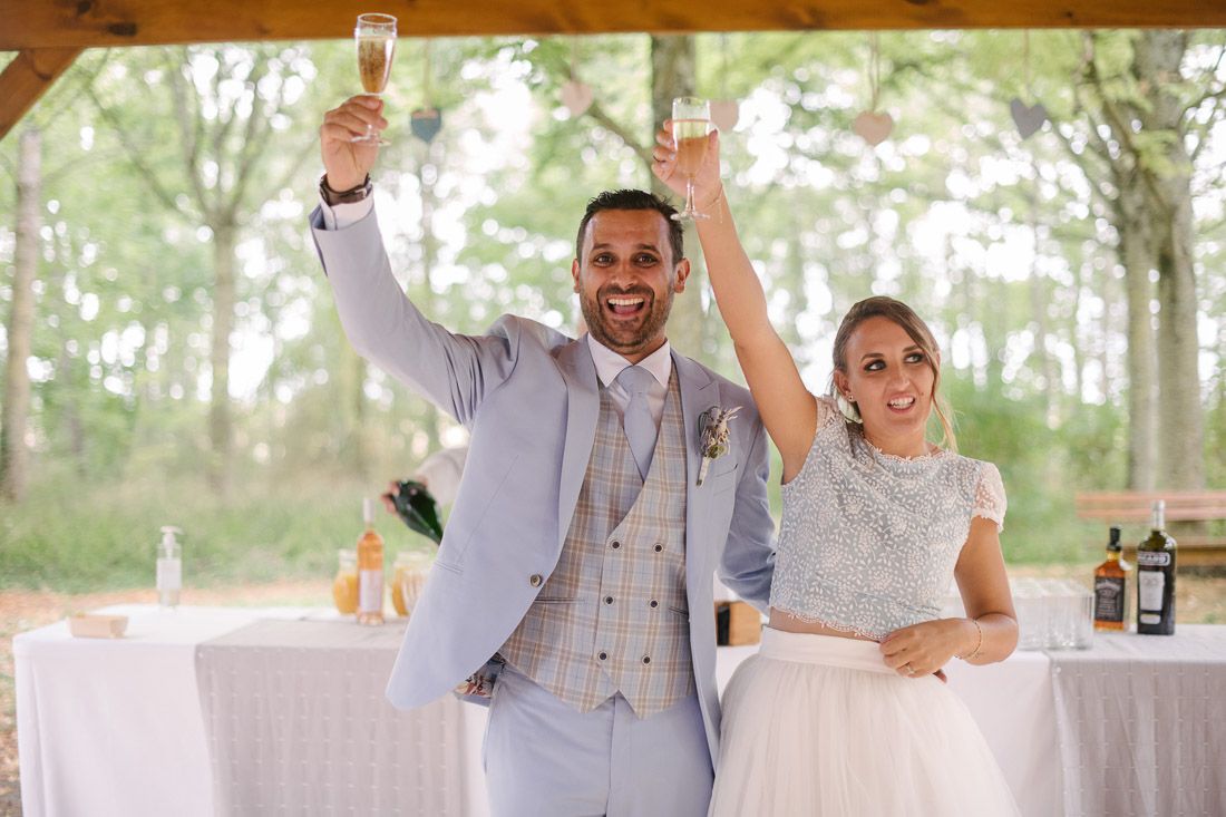 Newlyweds raise champagne glasses in celebratory toast at elegant outdoor wedding reception.