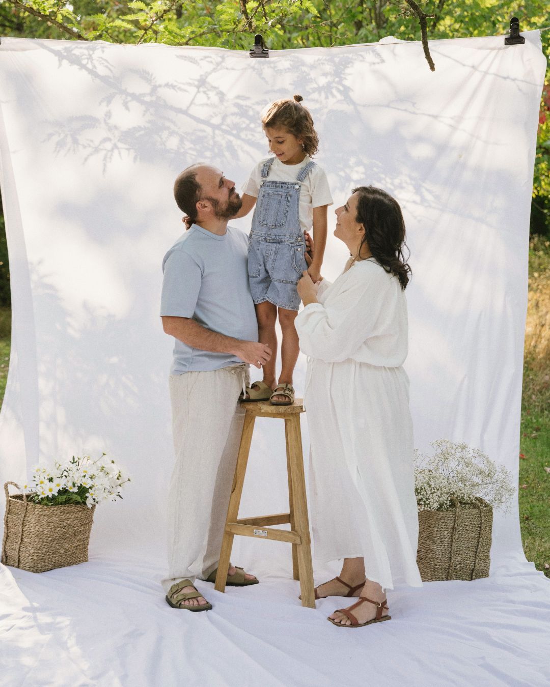 Family with toddler on stool posing outdoors against white backdrop.