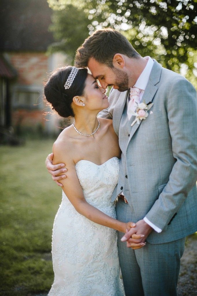 Bride and groom share a tender forehead touch in warm golden light on their wedding day.