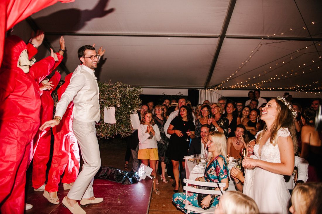 Wedding guests watch entertainer in red costume perform on dance floor at festive tent reception.