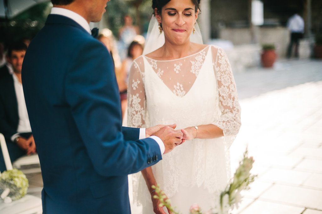 Bride smiling as groom places wedding ring on her finger during intimate outdoor ceremony.