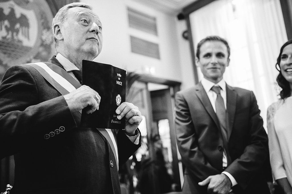Black and white photo of an official in a sash holding a document at a wedding ceremony.
