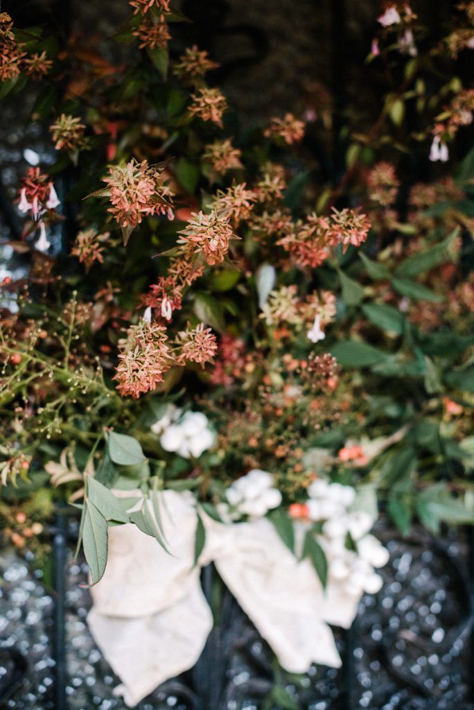 Rustic wedding floral arrangement with red berries, greenery, and white ribbon bow.
