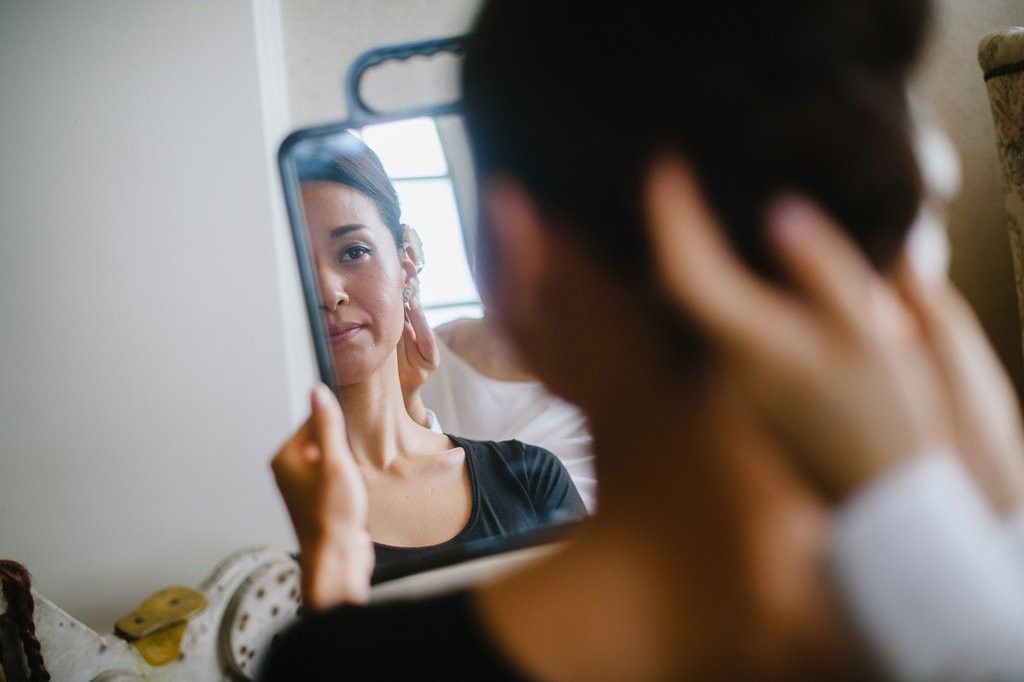 Bride checking her appearance in a handheld mirror while styling her hair before the wedding.
