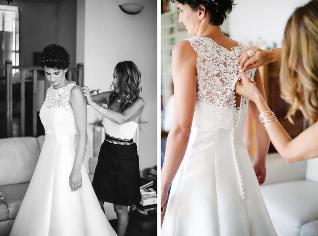 Black and white photo of bride getting wedding dress buttoned up by bridesmaid.