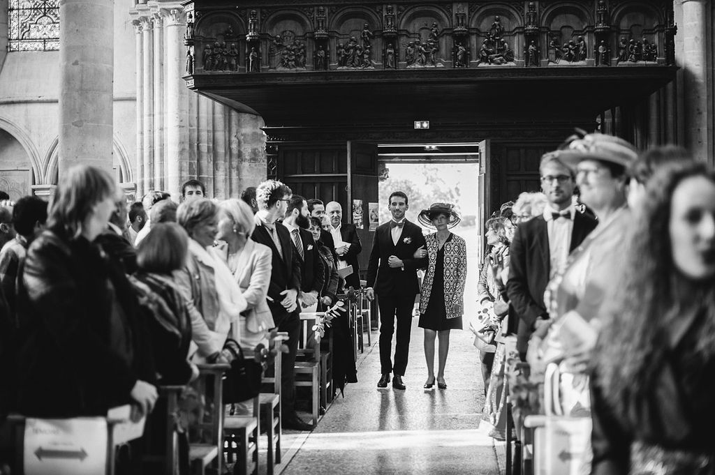 Guests walking down church aisle during wedding ceremony in black and white photo.
