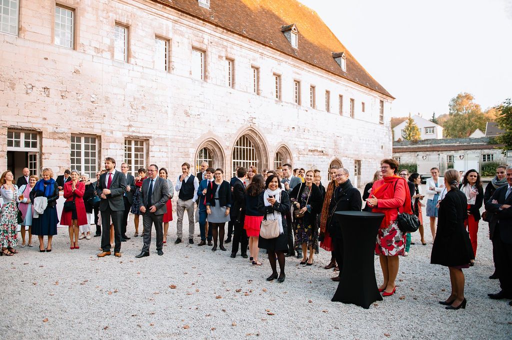 Wedding guests gathered outdoors listening to a speech at an elegant historic venue.