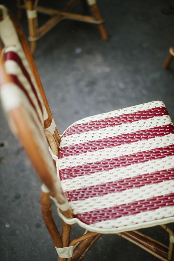 Close-up of a vintage wicker chair with red and white striped woven seat in a Parisian cafe.