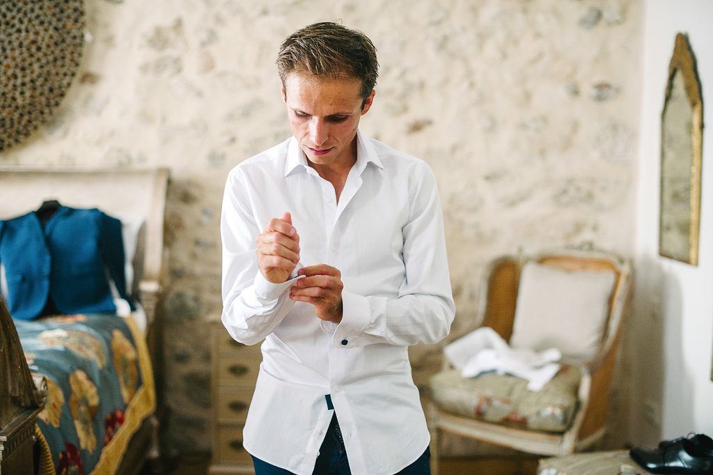 Groom in white dress shirt fastening cufflinks while getting ready for wedding ceremony.