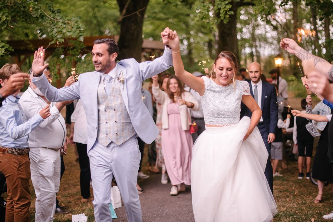 Joyful bride and groom dancing at outdoor wedding reception, guests celebrating with raised hands around them.