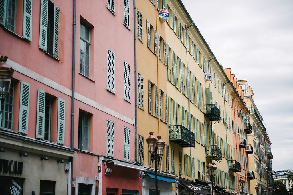 Colorful pastel-painted buildings with green shutters lining a street in Nice, France.