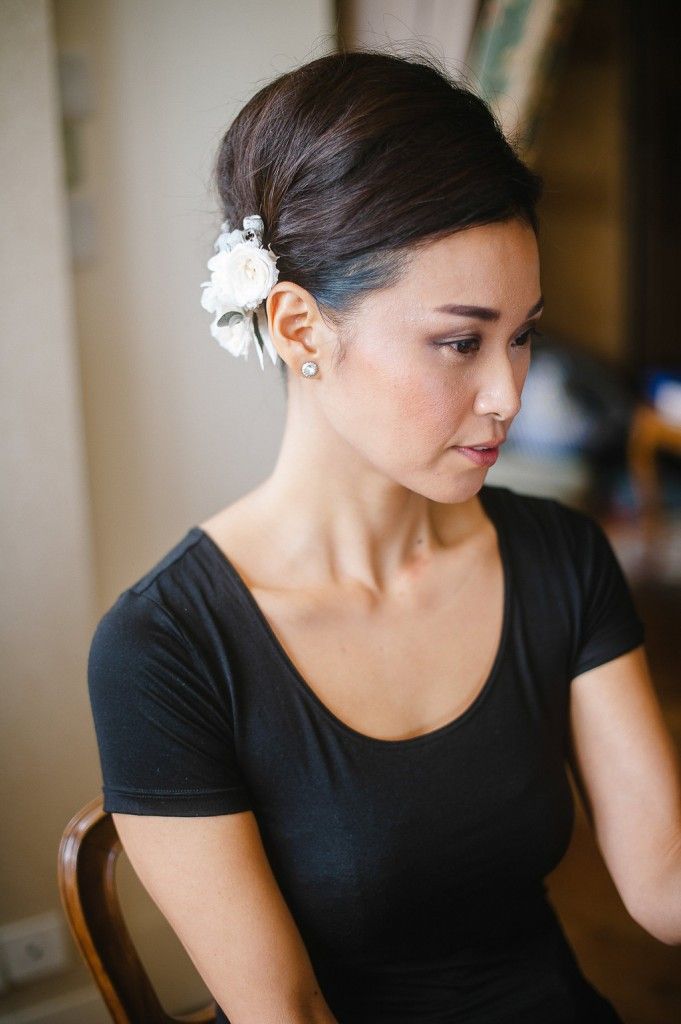 Bride with elegant updo adorned with white flower accessory wearing a black top before wedding.