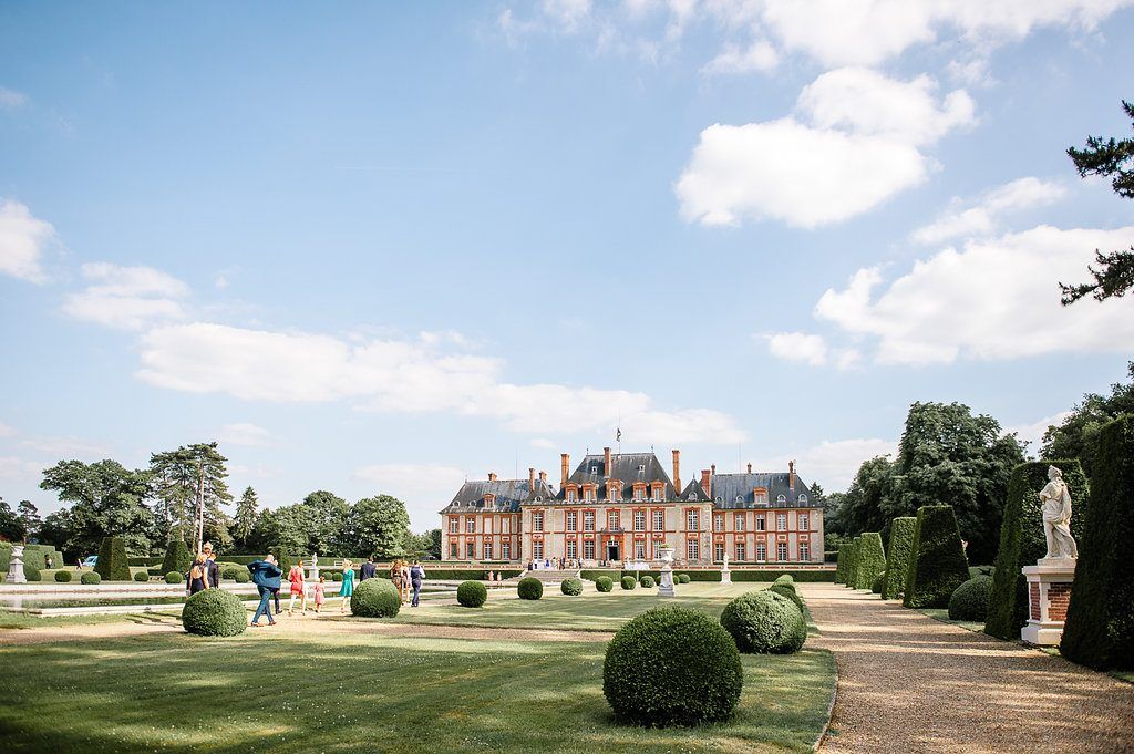 Grand French chateau wedding venue surrounded by manicured gardens and topiary under blue sky.