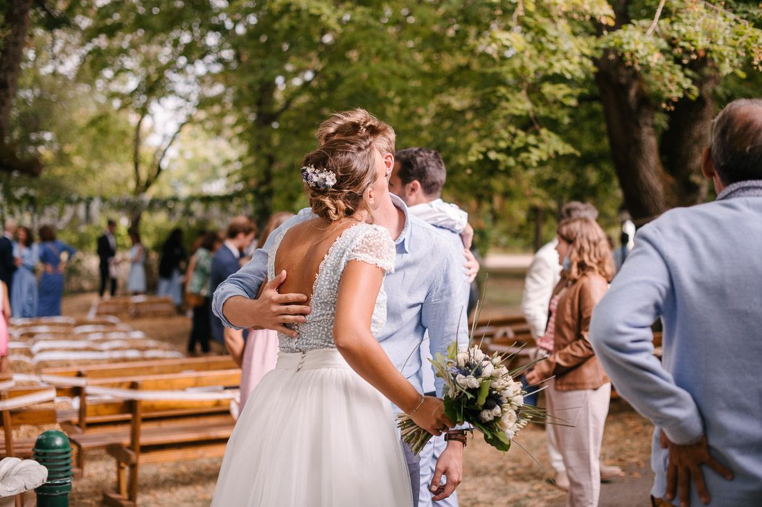 Bride and groom embrace and kiss after outdoor wedding ceremony surrounded by guests seated on wooden benches.