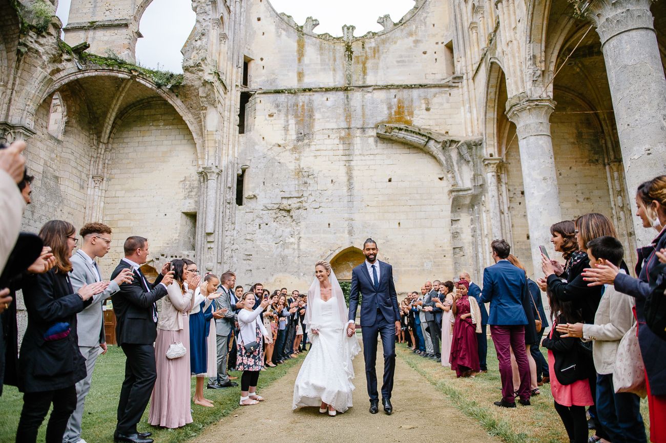 Bride and groom exit ceremony through cheering guests at a stunning historic stone ruins wedding.