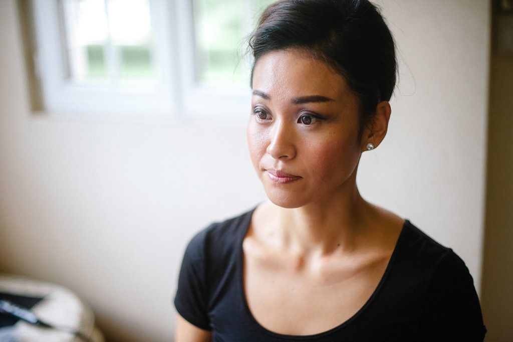 Young Asian woman in black top gazing thoughtfully to the side in a softly lit room.