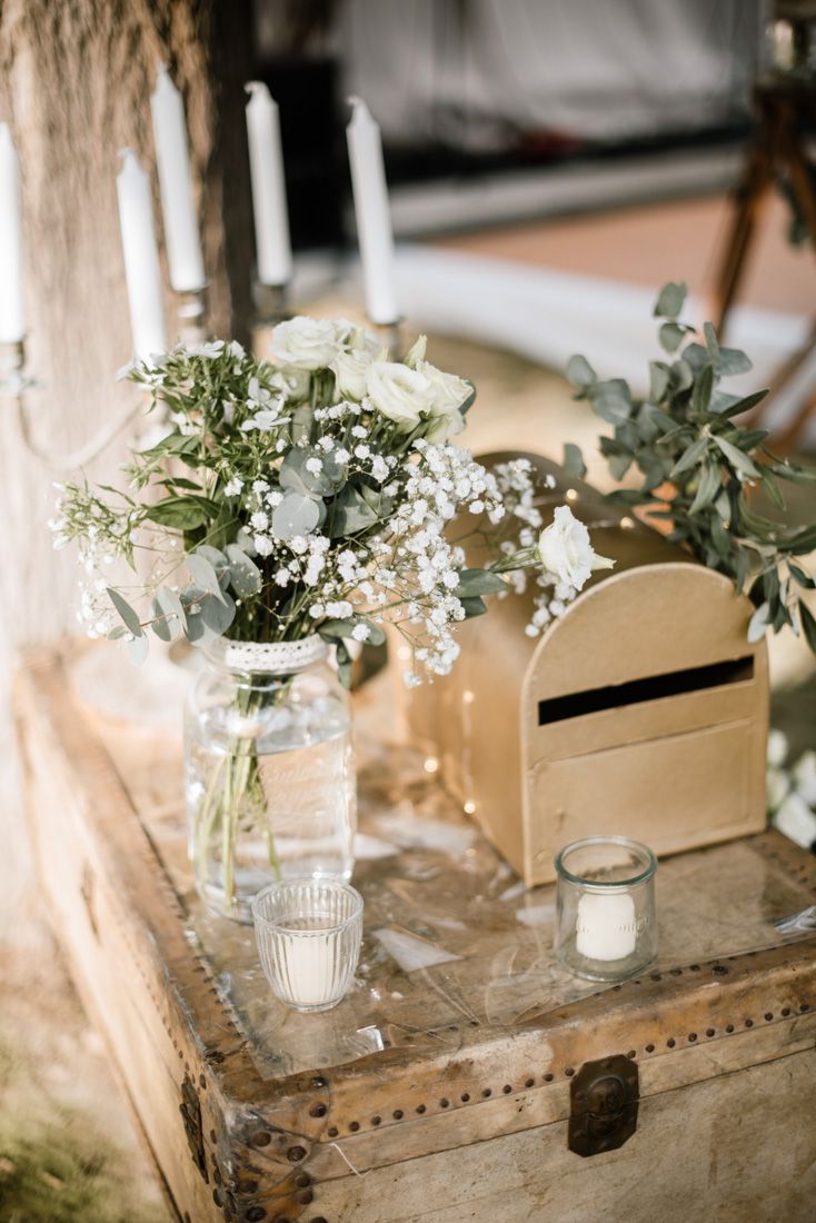 Rustic wedding decor with white flowers, candles, and a wooden card box on a vintage trunk.