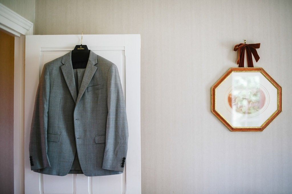 Gray groom suit jacket hanging on door beside octagonal framed picture on wall.