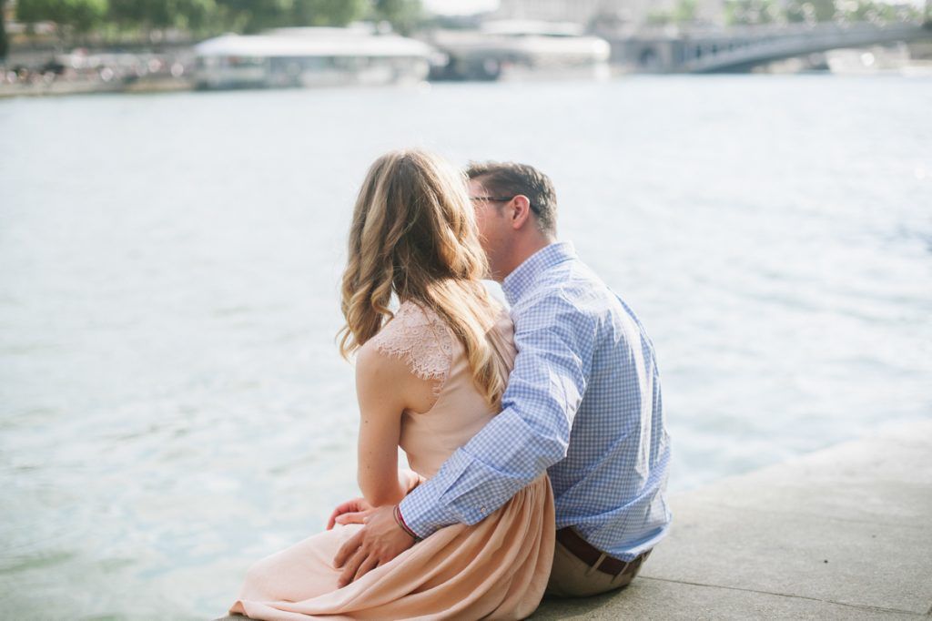 Couple sitting closely together on the banks of the Seine River in Paris, sharing a quiet moment.