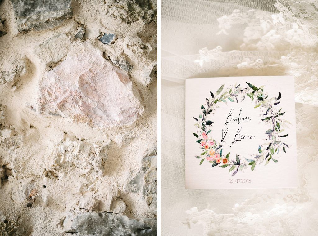 Wedding invitation with floral wreath design displayed next to rustic stone wall.