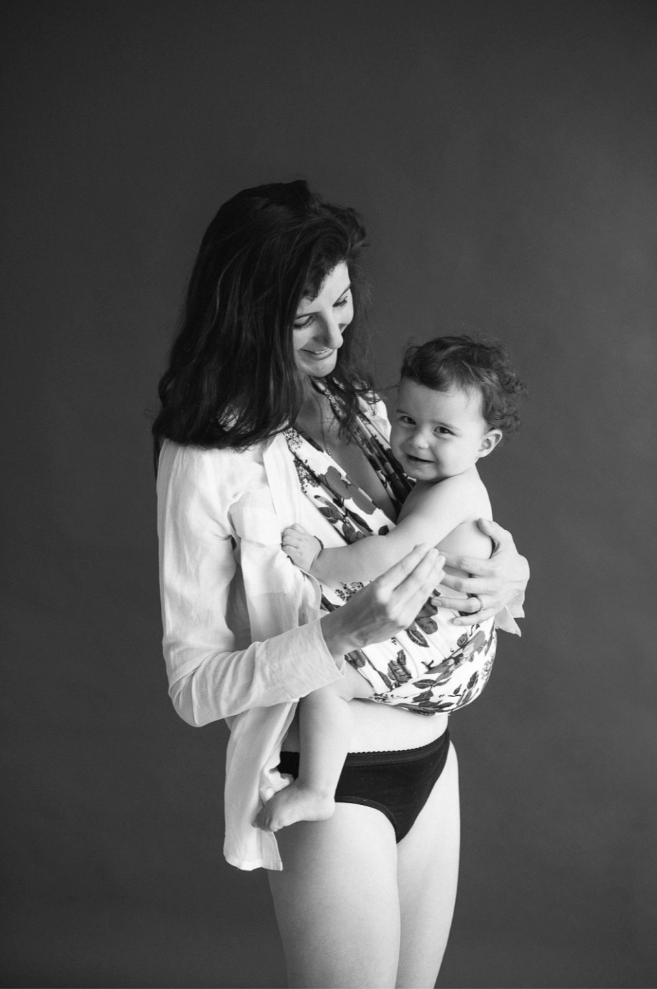 Black and white photo of a smiling brunette mother holding her happy laughing toddler child.