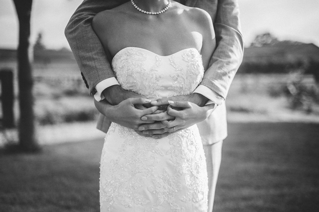 Black and white close-up of groom embracing bride in strapless lace wedding gown.