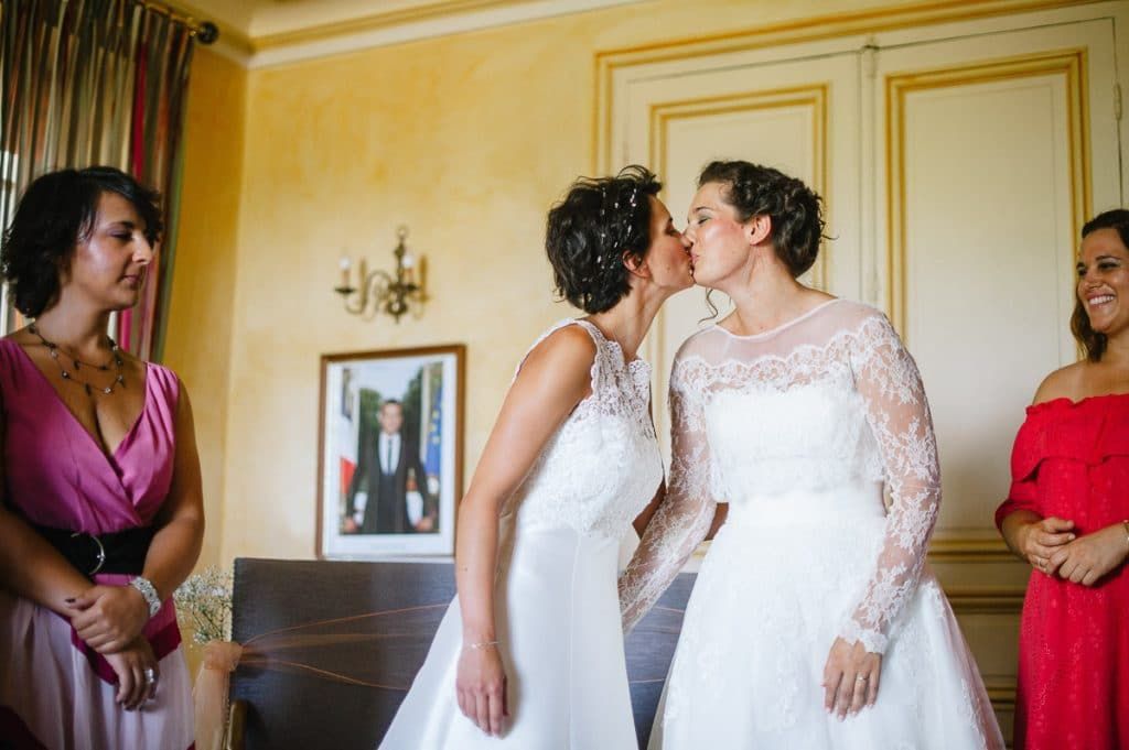 Two brides sharing a kiss during their wedding ceremony indoors.
