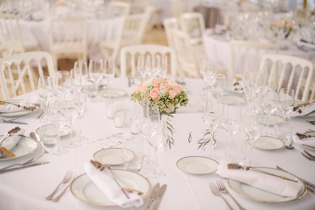 Romantic wedding reception tables with white linens, crystal glassware, and soft pink floral centerpieces.