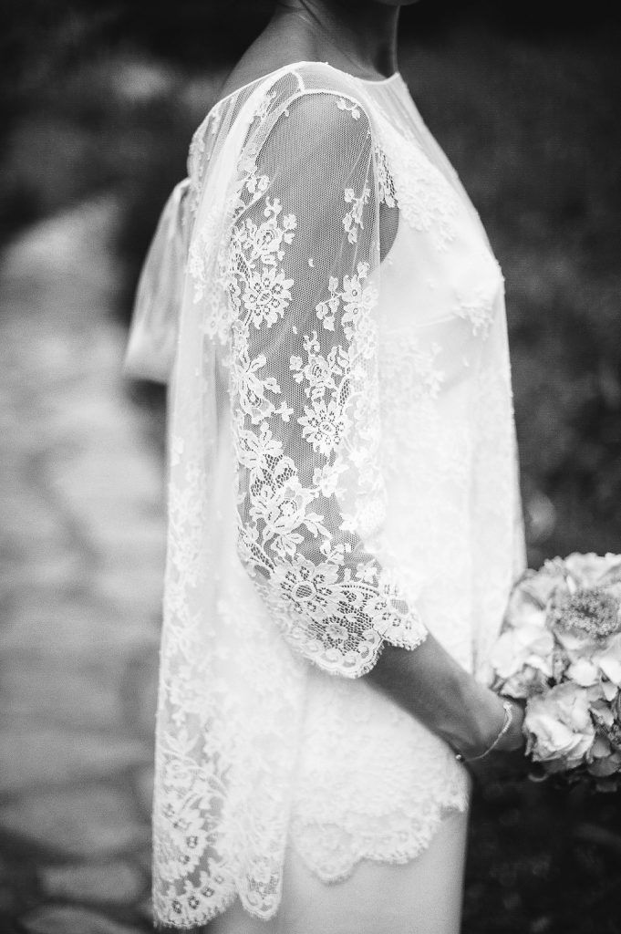 Black and white detail of bride's elegant lace wedding dress sleeves and bouquet.