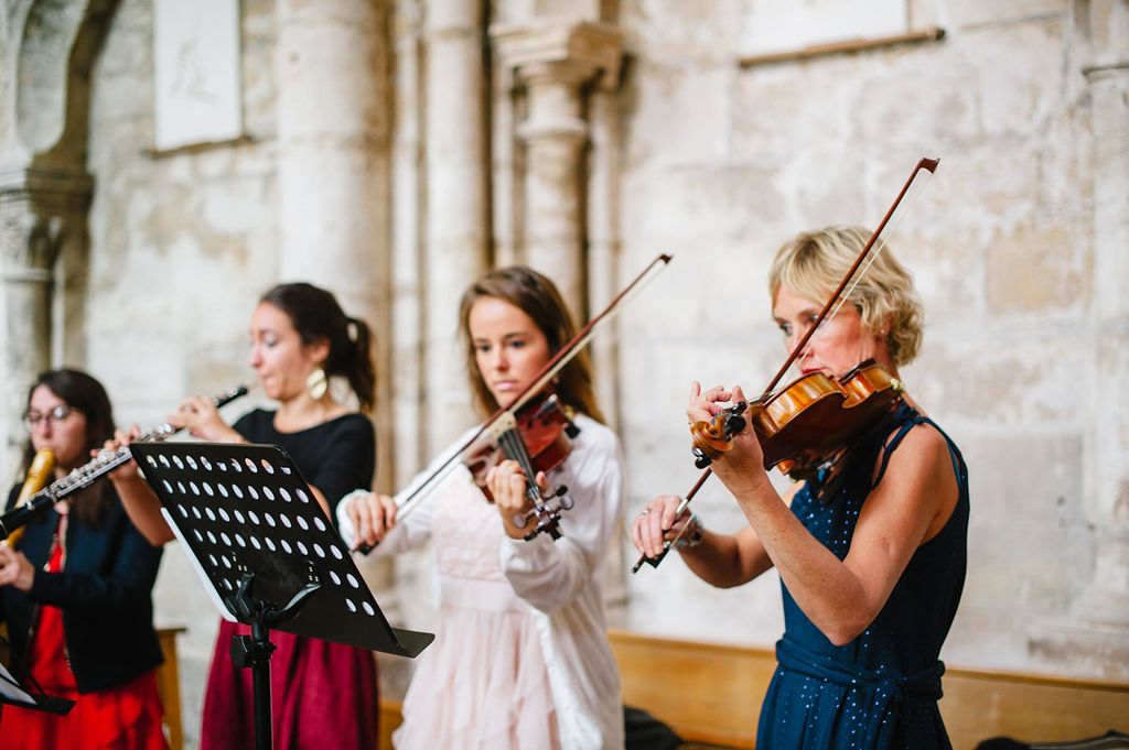 Three female musicians play violin and flute during a wedding ceremony inside a beautiful stone church.