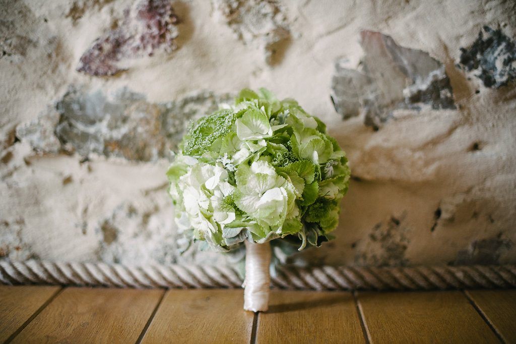 Elegant bridal bouquet of green hydrangeas and white flowers against rustic stone wall.