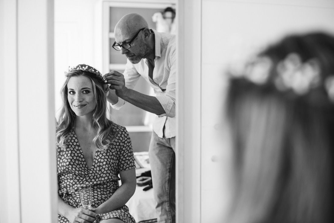 Black and white photo of a bride having a floral crown placed by a stylist, reflected in a mirror.