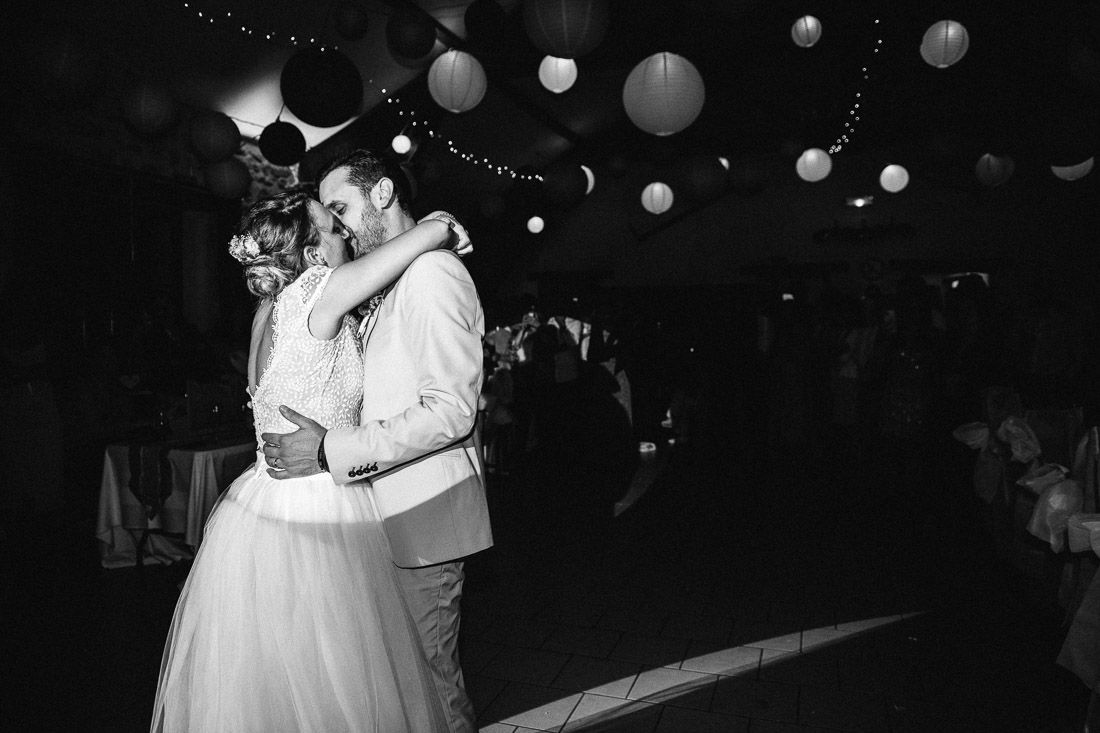 Black and white photo of bride and groom sharing first dance under paper lanterns at wedding reception.