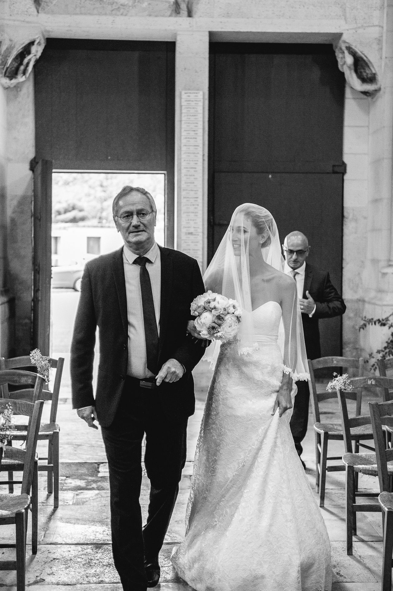 Black and white photo of bride walking down the aisle with her father at an elegant church wedding ceremony.